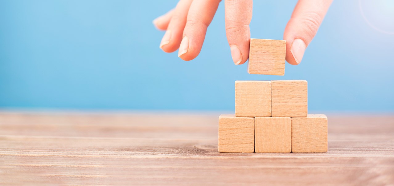 A person placing a building block at the top of a block pyramid.
